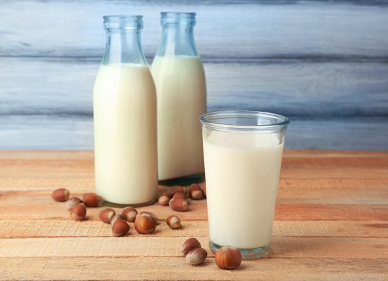 Using Flavours for Drinks. A glass and two bottles of Hazelnut milk with loose hazelnuts strewn across the table.